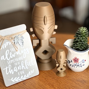 May include: A wooden sign with the text "There is always something to be thankful for" with a decorative twine bow and a metal leaf. Two gold-colored decorative statues and a white pitcher with a green succulent plant.