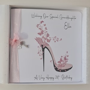 May include: A white card with pink ribbon and a silver key charm. The card has a pink high heel shoe with butterflies and the text "Wishing Our Special Granddaughter Elle A Very Happy 21st Birthday."