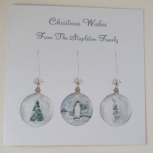 May include: A Christmas card with the text "Christmas Wishes From The Stapleton Family" and three watercolor illustrations of ornaments with a pine tree, a penguin, and a flower inside.