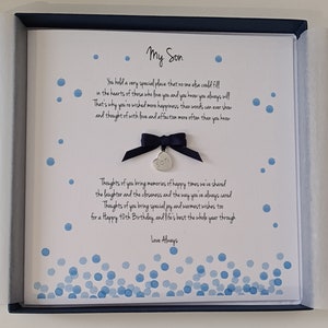 Peut inclure: Une carte blanche avec des points bleus en aquarelle et un charme argenté avec le mot "fils" dessus. La carte contient un poème sur un fils et dit "Mon Fils" en haut et "Amour Toujours" en bas.