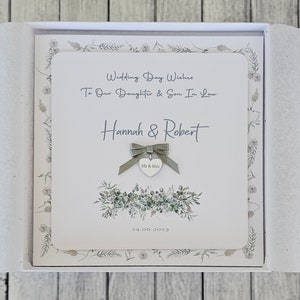 May include: A white card with a green floral design and the text "Wedding Day Wishes To Our Daughter & Son In Law Hannah & Robert Mr & Mrs 24.06.2023"