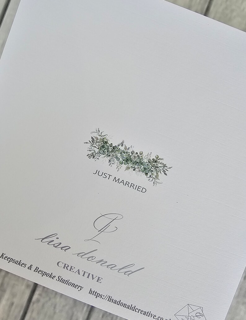 May include: A white card with a green leafy floral wreath with the text "Just Married" in the center. Below the wreath is a cursive signature that reads "Lisa Donald Creative" with the website address "https://lisadonaldcreative.co.uk".