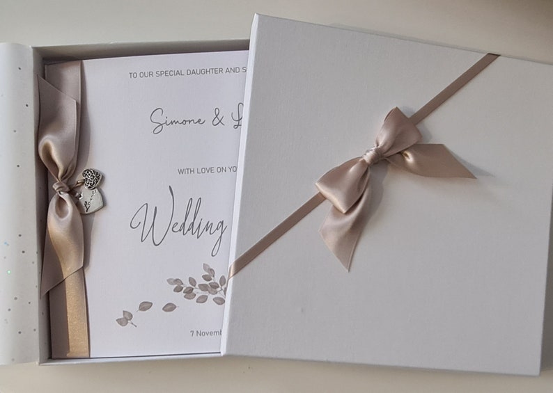 May include: A white box with a beige ribbon and bow. The box contains a white card with the text "To our special daughter and son, Simone & [unclear text], with love on your wedding, 7 November".