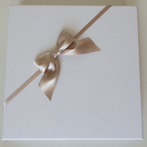 May include: A white gift box with a diagonal beige satin ribbon tied in a bow.