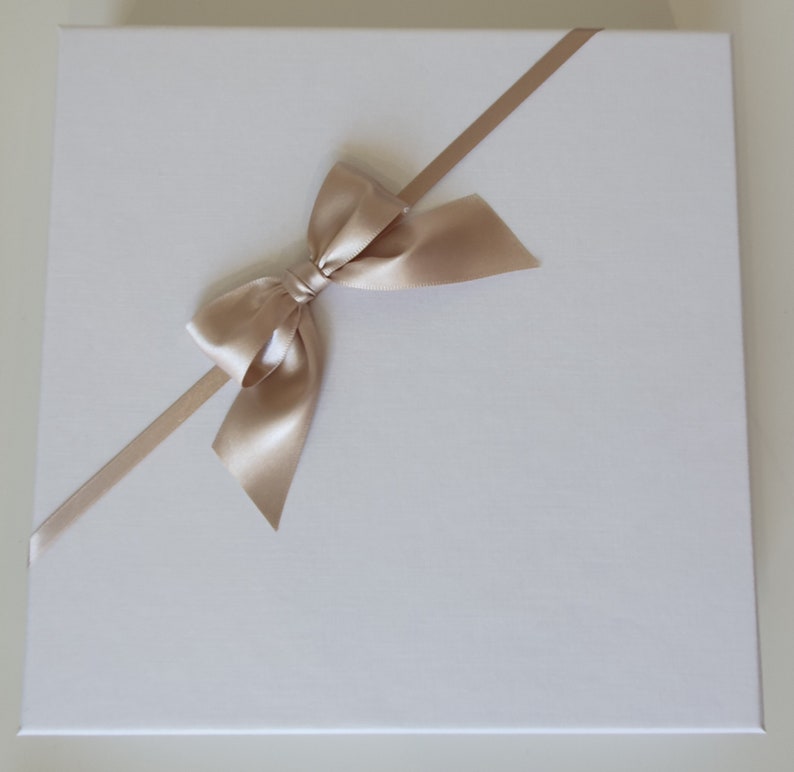 May include: A white gift box with a diagonal beige satin ribbon tied in a bow.