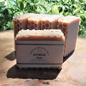 May include: A stack of four honey soap bars with a honeycomb design. The soap bars are wrapped in brown paper with a label that reads "Temple of the Seven Dolls Just Honey Soap Soap Company LLC net wt. approx. 4.5 ounces".