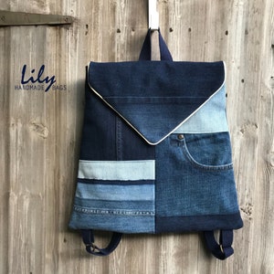 May include: A blue denim backpack with a white trim and a patchwork design. The backpack has a flap closure and adjustable straps. The text "lily HANDMADE BAGS" is visible on the left side of the image.