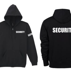 Op de afbeelding: Zwarte hoodie met rits, met het woord "SECURITY" in wit gedrukt op de rug en de linkermouw.