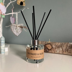 May include: A clear glass bottle diffuser with black reeds and a brown label that reads "Rhubarb & Rose" and "Stay - LavenderBloomsUK".