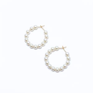 May include: A pair of hoop earrings featuring a circular gold-tone wire frame adorned with a series of small, round, white pearls arranged evenly around the entire circumference of each hoop, secured with a simple wire closure mechanism.