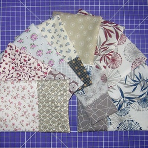 Könnte beinhalten: Eine Sammlung von Stoffquadraten in verschiedenen Mustern und Farben, darunter florale, geometrische und abstrakte Designs. Die Stoffe sind fächerförmig auf einer violetten Schneidematte angeordnet.