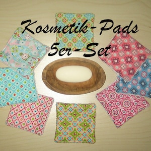 Könnte beinhalten: Ein Set mit fünf bunten, gemusterten Kosmetikpads aus Stoff. Die Pads sind quadratisch und haben einen weißen Rand. Der Text "Kosmetik-Pads 5er-Set" ist im Bild sichtbar.