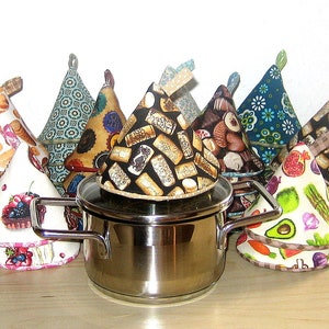 Könnte beinhalten: Eine Sammlung von neun bunten Topflappen in verschiedenen Mustern, darunter Obst, Gebäck und Kork. Die Topflappen sind kegelförmig und haben einen Schlaufe. Ein Topf aus Edelstahl mit einem Glasdeckel befindet sich in der Mitte des Bildes.