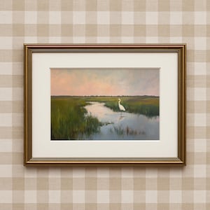 Op de afbeelding: Een ingelijst landschapsschilderij met een witte zilverreiger in een moerassige waterweg. Het kunstwerk heeft een gouden lijst en een witte passe-partout. De schildering toont een serene scène met groen moerasgras, een reflecterend wateroppervlak en een kleurrijke zonsondergang.