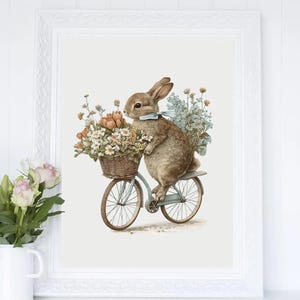 May include: A framed watercolor print features a brown rabbit riding a light blue bicycle with a wicker basket filled with flowers. The rabbit wears a blue bow. The artwork has a vintage, whimsical style, perfect for nursery decor.