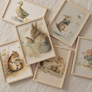 May include: A collection of framed watercolor prints featuring charming animal illustrations. The artwork includes a duck with ducklings, a mouse with a dandelion, a rabbit family reading, a kitten, and a mother mouse with her child. The frames are light wood.