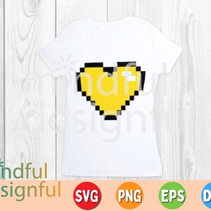 May include: White t-shirt featuring a pixelated yellow heart with black outlines. The shirt has a crew neck and short sleeves. The words "mindful designful" are printed at the bottom left. The image also includes SVG, PNG, EPS, and DXF icons.