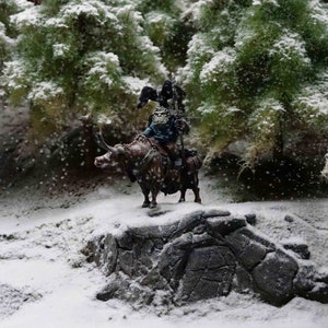 Peut inclure: Une figurine miniature d'un guerrier chevauchant un yak, sur fond de forêt enneigée. La figurine porte une armure et tient une arme. Le yak est brun et blanc avec des cornes. La scène est recouverte de neige.