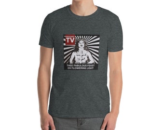 May include: A dark heather grey t-shirt with a black and white graphic print of a woman with a cross on her chest. The graphic also includes the text "PSYCHIC TV" and "THEE FABULOUS FEAST OV FLOWERING LIGHT".