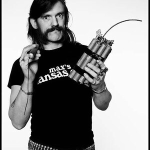 May include: A black and white photo of a person wearing a black t-shirt with the text "max's ansas" printed on it. The person is holding a bundle of dynamite with a lit fuse.