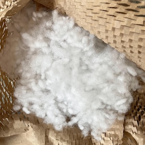 May include: A close-up of white stuffing material inside a brown paper packing material. The stuffing is loose and fluffy, and the paper is crinkled and torn.