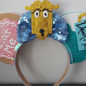 May include: Alice in Wonderland themed mouse ears with a blue and gold bow, a cookie with "Eat Me" written on it, and a bottle with "Drink Me" written on it.