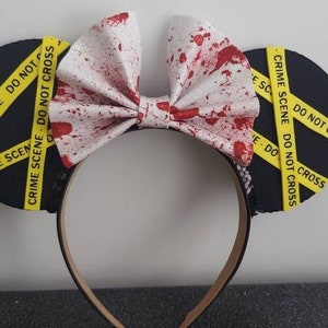 May include: Black mouse ears with a white bow covered in red splatter paint. The ears are decorated with yellow caution tape that reads "CRIME SCENE DO NOT CROSS".