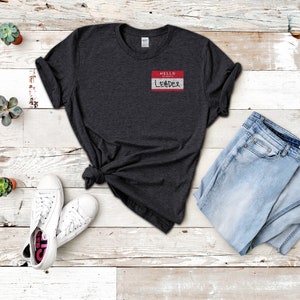 May include: A dark gray t-shirt with a white name tag that says "HELLO MY NAME IS LEADER" in red lettering.