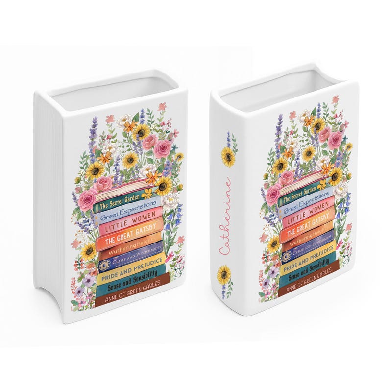 May include: White ceramic book-shaped vase decorated with a floral arrangement of sunflowers, roses, and other flowers. The vase features book titles like "The Secret Garden" and "Pride and Prejudice". The name "Catherine" is written on the side.