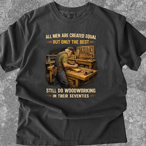 Könnte beinhalten: Dunkelgraues T-Shirt mit dem Text "ALL MEN ARE CREATED EQUAL BUT ONLY THE BEST STILL DO WOODWORKING IN THEIR SEVENTIES." Das Shirt zeigt einen Tischler an einer Werkbank mit Werkzeugen.