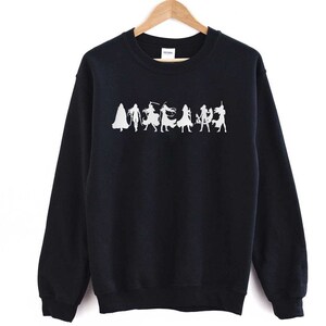 May include: Black sweatshirt with a white silhouette of a group of people in various poses. The people are wearing long robes and appear to be holding swords or other weapons.