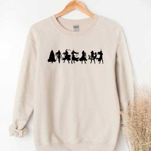 May include: A beige sweatshirt with a black silhouette of a group of people in various poses. The silhouettes are in a line across the front of the sweatshirt.