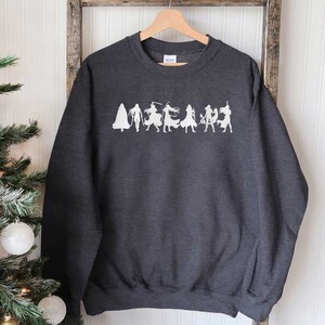 May include: A dark gray sweatshirt with a white graphic of a group of figures in silhouette. The figures are arranged in a line and appear to be wearing different costumes.