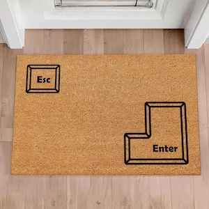 May include: A rectangular doormat in a light brown hue. It displays black outlines of the "Esc" and "Enter" keys from a computer keyboard. The word "Enter" is written in black within the key outline, a fun welcome mat.