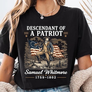 May include: Black t-shirt featuring a patriotic graphic. The design includes an illustration of a man in historical attire holding a rifle, standing before a flag. Text reads "Descendant of a Patriot" and "Samuel Whitmore 1759-1802".