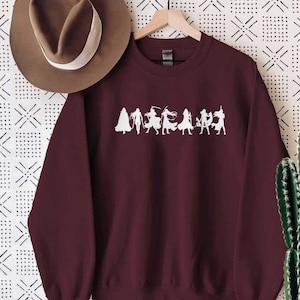 May include: Burgundy sweatshirt with a white silhouette of a group of people wearing fantasy costumes. The text "MEGAMIND" is printed below the silhouettes.
