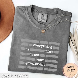 Puede incluir: Una taza de cerámica blanca con un asa negra y el texto "But First, Coffee" en negrita negra. La taza está sobre una superficie de madera. La taza mide 10 cm de alto.