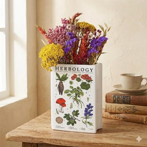 May include: A white rectangular vase with the word "HERBOLOGY" printed on it, filled with colourful dried flowers. The vase has botanical illustrations and the text "HOGWARTS SCHOOL OF WITCHCRAFT AND WIZARDRY".