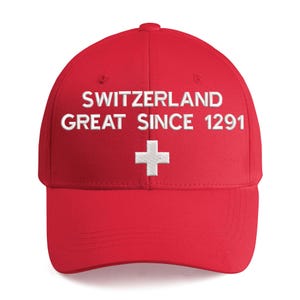 Könnte beinhalten: Eine leuchtend rote Baseballkappe mit weißem Sticktext, der SWITZERLAND GREAT SINCE 1291 lautet, platziert über einem weißen Schweizer Kreuz. Die Kappe hat eine strukturierte Krone, einen gebogenen Schirm und einen Knopf oben.