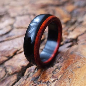 May include: A handcrafted ring featuring a glossy black exterior with a vibrant red wood inlay. The ring is made of wood and has a smooth, polished finish. This unique ring is a stylish accessory.