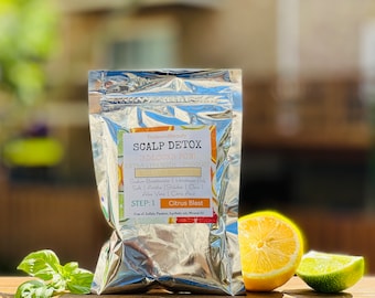 May include: A silver pouch with a white label that reads "PrideandBeauty SCALP DETOX ADLOCKS POW! EXTRA STRENGTH PRODUCI Sadun Beeplonate | Himalayan Dak Sale | Anthe Shhaha C Also Vona Ctric And STEP: 1 Citrus Blast Tre" and a graphic of a citrus fruit slice. The pouch is sitting on a wooden surface with a lemon, lime, and basil.