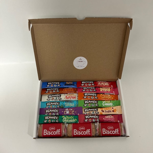 May include: An open cardboard box filled with a variety of individually wrapped flavored coffee sachets. The sachets are labeled "Beanies" and feature different flavors, including "Nulty Hazelnut", "Orange", "Popcorn", "Coconut Delight", "Double Choc", "Mint Chocolate", "Almond", "Deuch", "Caramel", "Cream", "Fudge", and "Chocolate Raspberry". Three Biscoff cookies are visible at the bottom of the box.