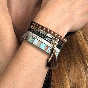 Può includere: Un set di braccialetti colorati con un cinturino in pelle marrone e un fiocco dorato. I braccialetti hanno una varietà di motivi e trame, tra cui pelle di serpente, strisce e pois.