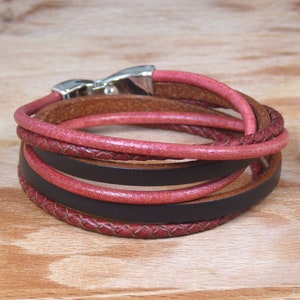 Op de afbeelding: Een meerlaags leren armband met een zilveren sluiting. De armband is gemaakt van een combinatie van bruine, zwarte en roze leren banden.