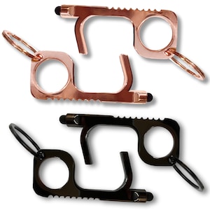 May include: Two copper-colored and two black no-touch door opener tools. Each tool has a finger hole, a hook, a stylus tip, and a keyring attachment. The copper tools have a shiny finish, while the black tools have a matte finish.