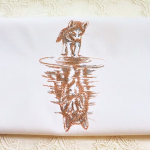 May include: A white kitchen towel with black stripes on the sides features an embroidered image of a brown and white wolf pup looking at its reflection in a pool of water.