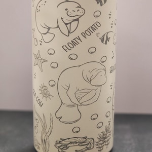 May include: A white insulated water bottle with a black and white design of manatees, sea turtles, starfish, and seaweed. The text "Floaty Potato" and "Sea Cow" are printed on the bottle.