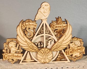 May include: Wooden Harry Potter-themed wall art featuring the Deathly Hallows symbol, the Hogwarts house crests (Gryffindor, Slytherin, Ravenclaw, Hufflepuff), and a snowy owl. The art is made of light-colored wood with intricate laser-cut details.