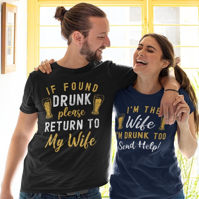 May include: A couple wearing matching t-shirts with a beer theme. The man's shirt says "If found drunk please return to my wife". The woman's shirt says "I'm the wife I'm drunk too send help!"