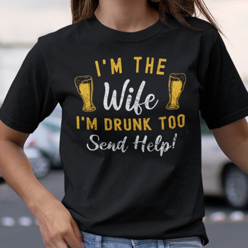 May include: Black t-shirt with a distressed white graphic that says "I'm the Wife I'm Drunk Too Send Help!" with two beer glasses on either side of the word "Wife".